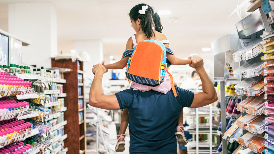 elementary school girl seen from behind riding on fathers shoulders while shopping in a retail store for back to school supplies