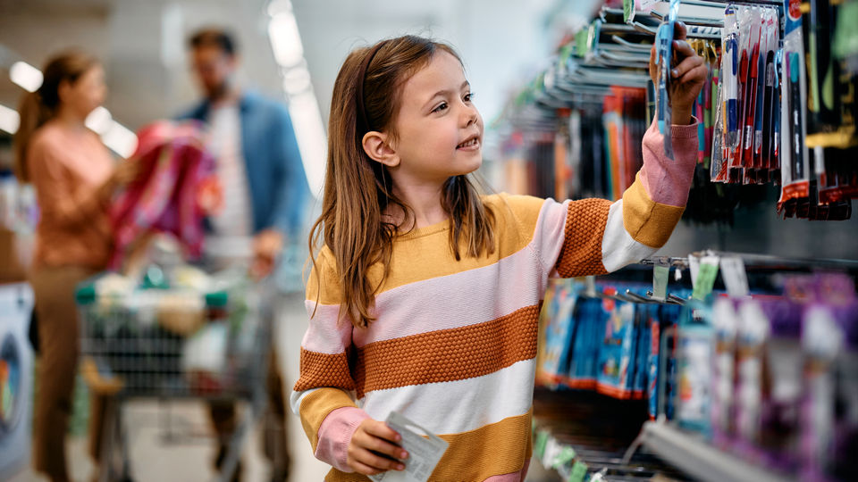young girl choosing school supplies in retail store while parents in the background look at backpacks