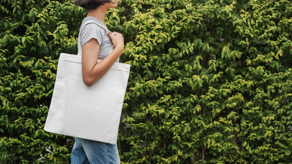 woman wearing jeans and t-shirt carrying cloth shopping bag  in front of greenery