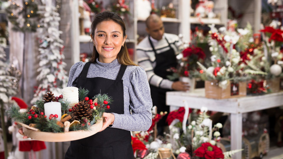 female retail store employee carrying holiday decoration items in holiday decoration store