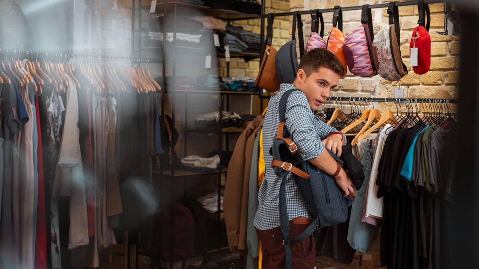 young male shoplifter in retail apparel store hiding items in a backpack