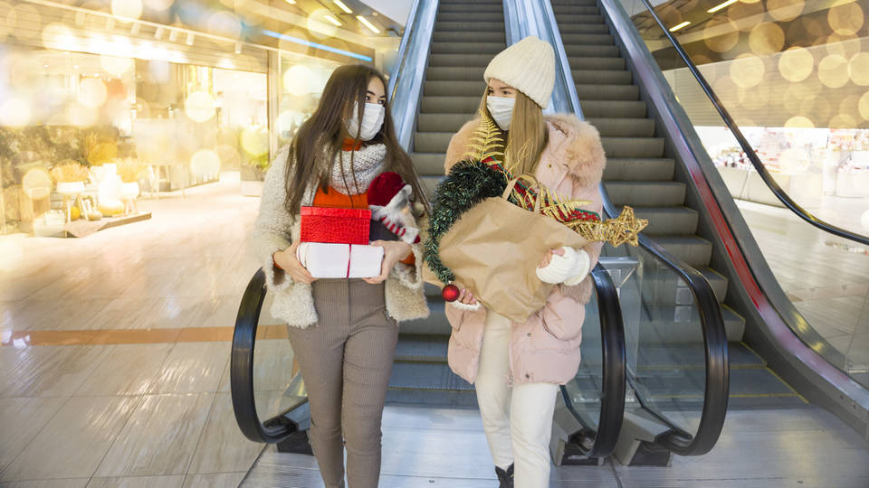 two masked female shoppers stepping off escalator in retail shopping center