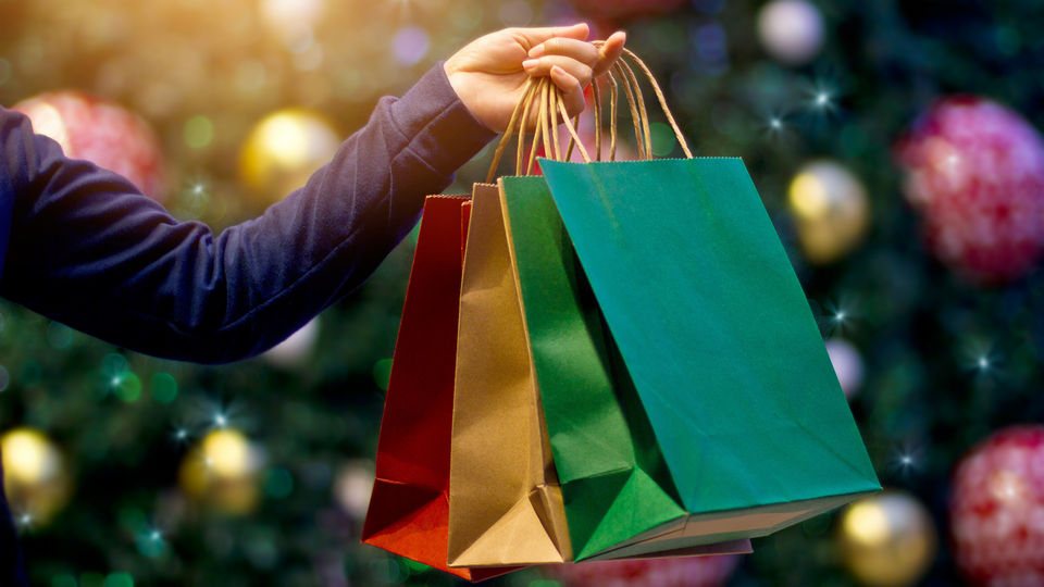 female hand holding festively colored retail shopping backs with decorated christmas tree in the background