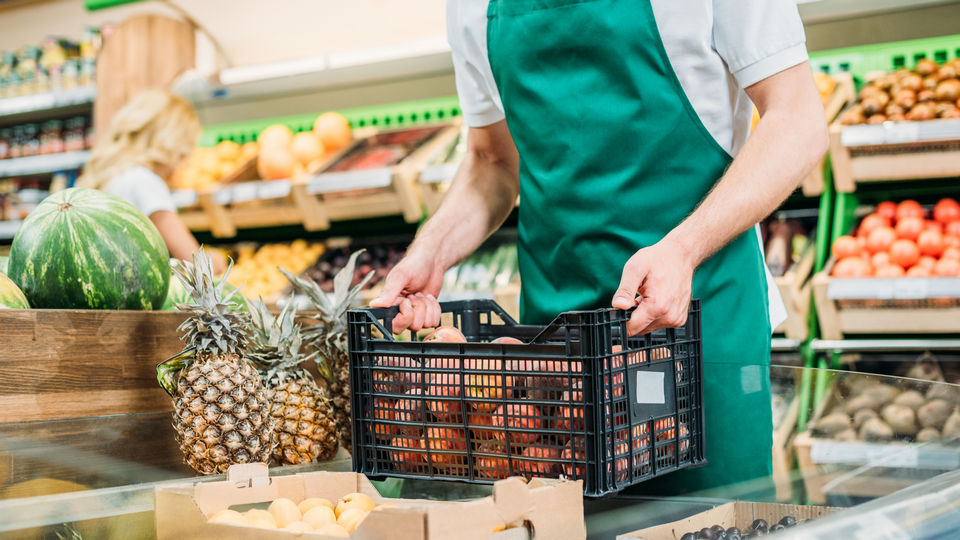 supermarket employee holding crate of fresh produce