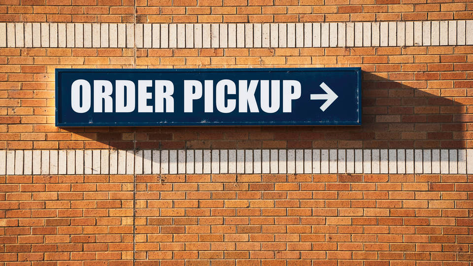 sign on retail store exterior brick wall says order pickup with arrow pointing to omnichannel fulfillment area