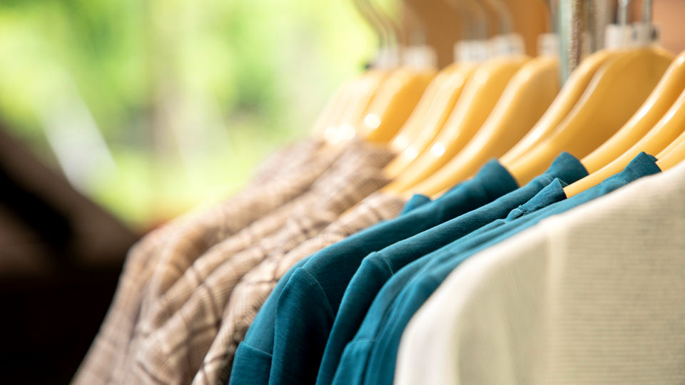 retail apparel store rack of sweaters with greenery and foliage visible in the background