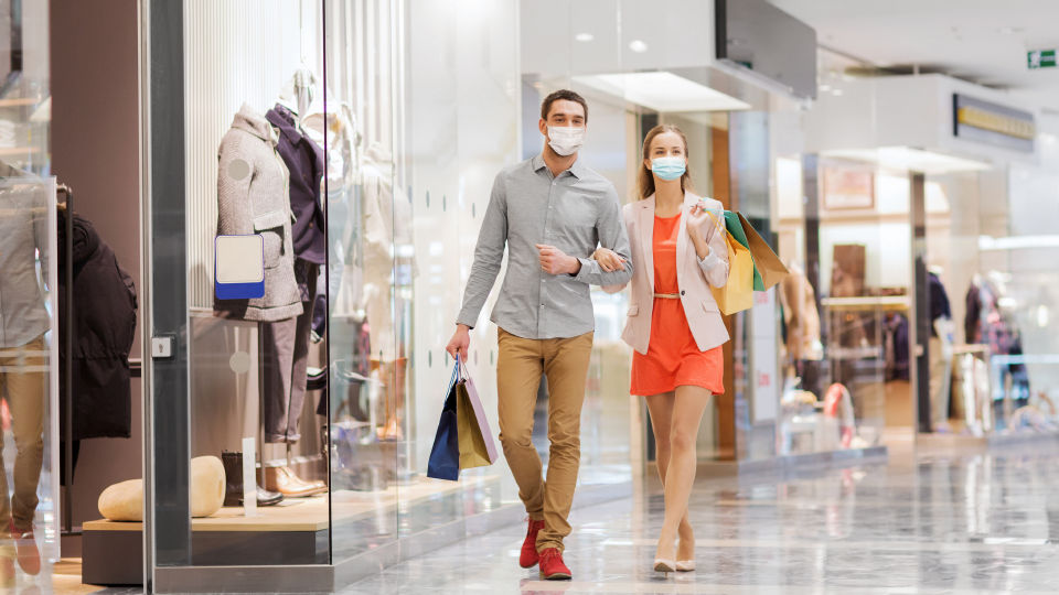 masked male and female shoppers walking through mall carrying purchases