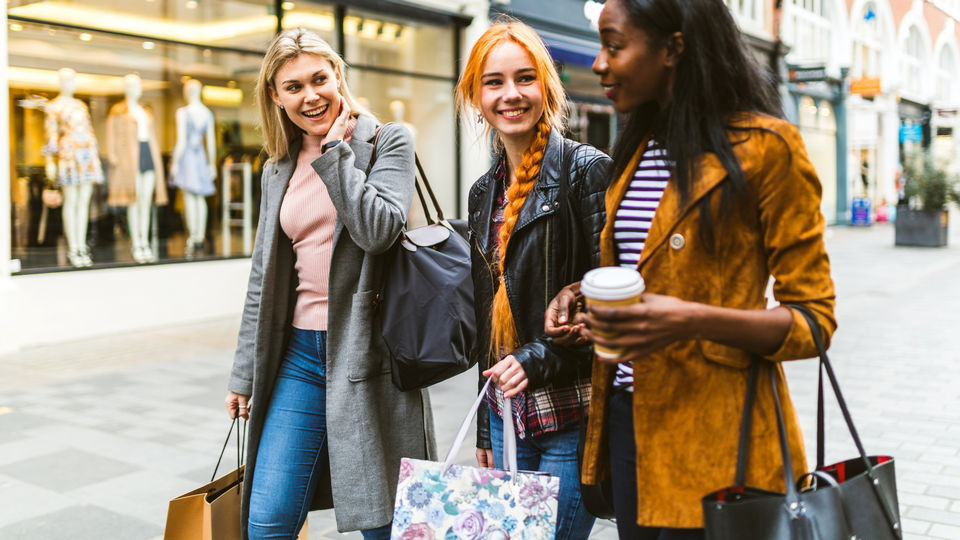 3 female shoppers chatting and carrying shopping bags while walking down the street in a retail shopping district