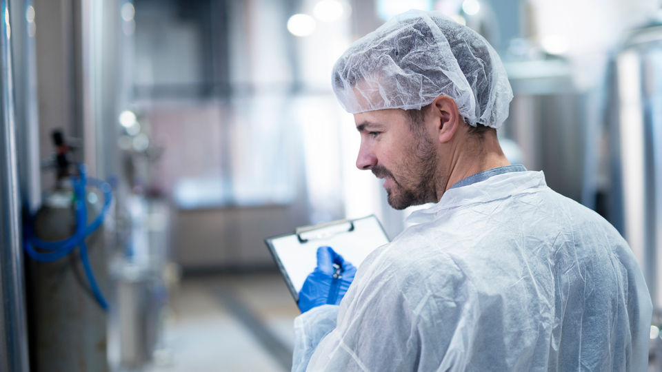 male worker in food factory wearing ppe inspects refrigerated machinery