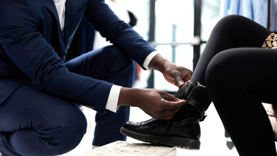 closeup view of man shoe store employee kneeling on floor helping woman retail customer try on a pair of boots