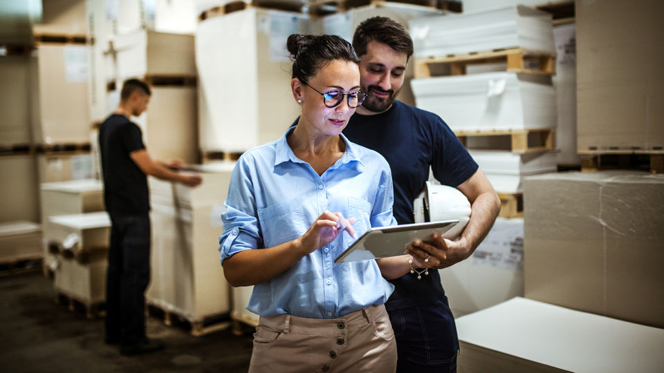 male and female retail warehouse workers reviewing inventory on electronic device