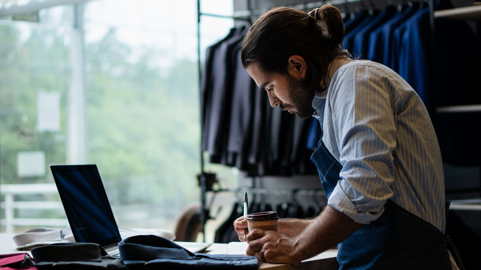 retail apparel store manager entering data on paper and in laptop