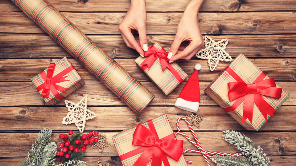 view from above of female hands wrapping assorted presents with holiday theme