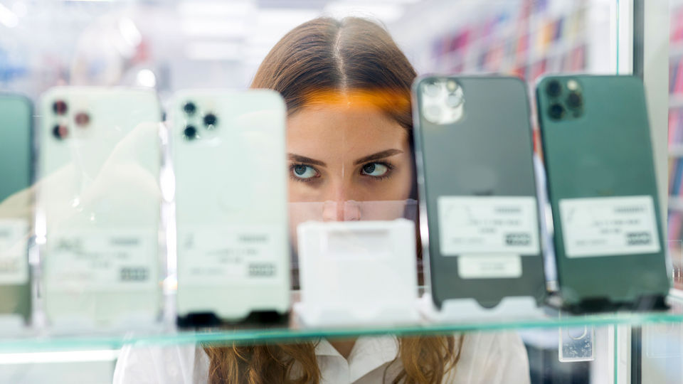 woman shoplifter face partially obscured by display of mobile phones in retail electronics store