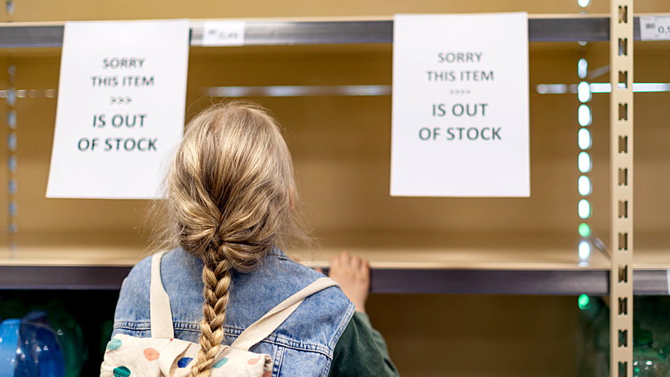 rear view of young girl shopper looking at empty shelves in retail store with signs saying this item is out of stock