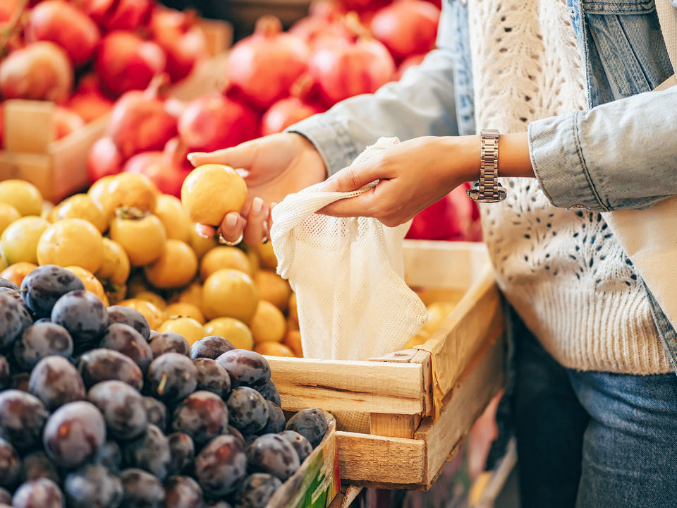 female hands choosing lemons from a produce display in a retail grocery store and putting them in an eco-friendly bag