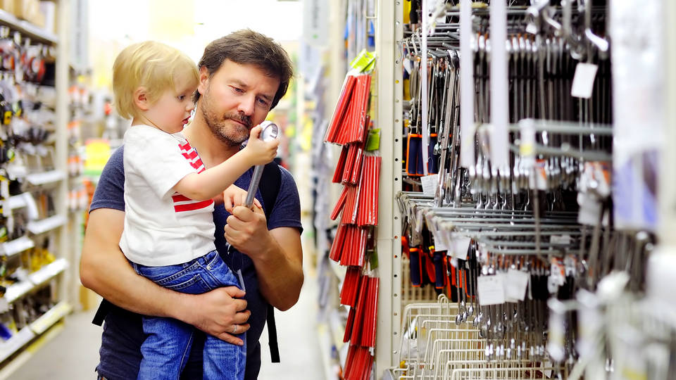 male shopper holding child and looking at tool display in retail hardware diy store