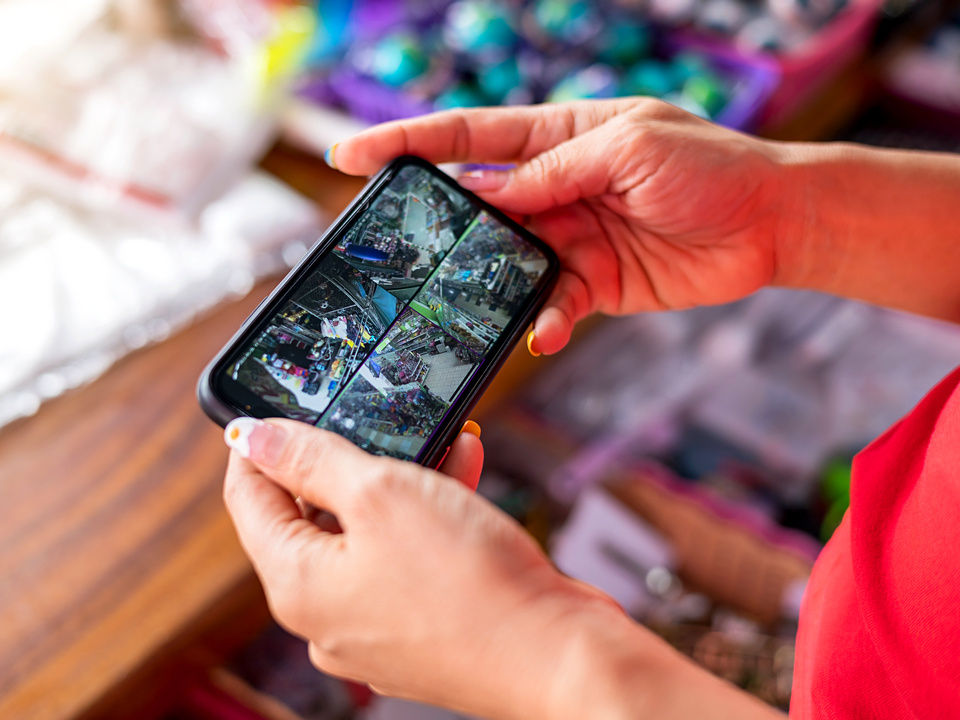 retail employee holding mobile phone displaying multiple camera views of the store