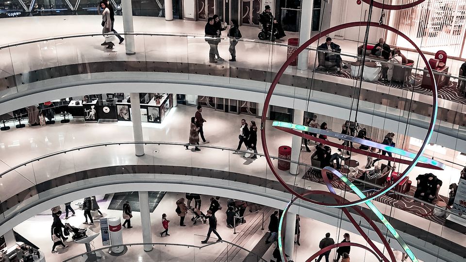 interior of multi-level shopping mall with many retail shoppers and a large hanging sculpture of interlocking rings