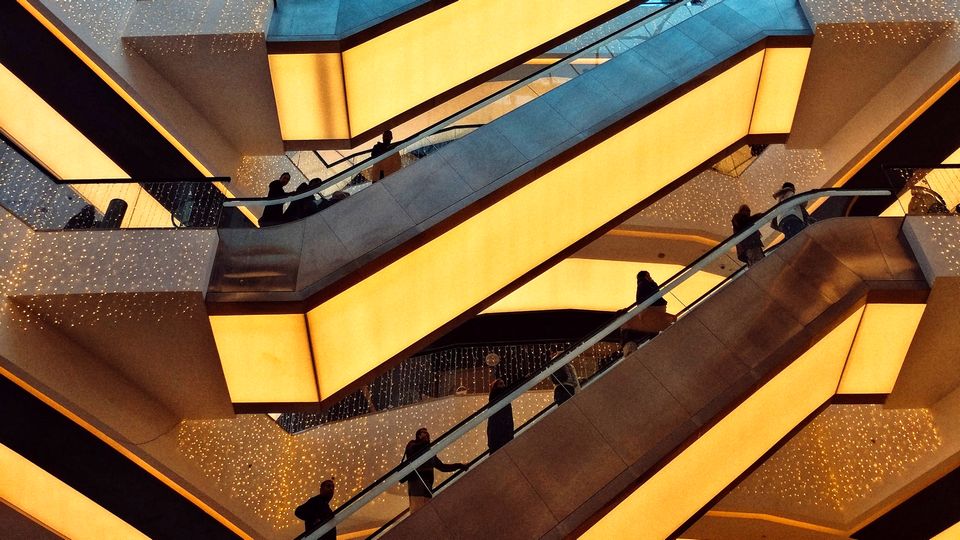 looking up in multi-level shopping mall at three flights of crowded escalators underlit with golden lighting