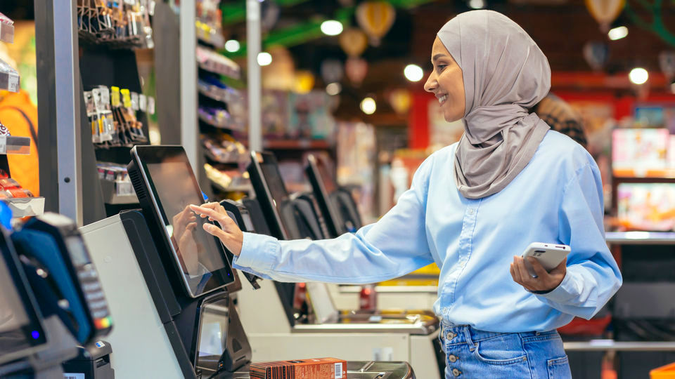 woman shopper in headscarf paying for her purchases at self-checkout counter of a retail grocery store