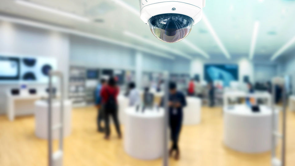 ceiling mounted ip video camera in retail store with blurred shopping activity in the background