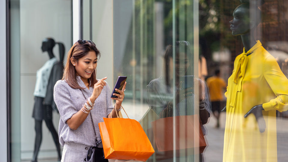 female shopper with shopping bags using mobile phone outside retail apparel store window