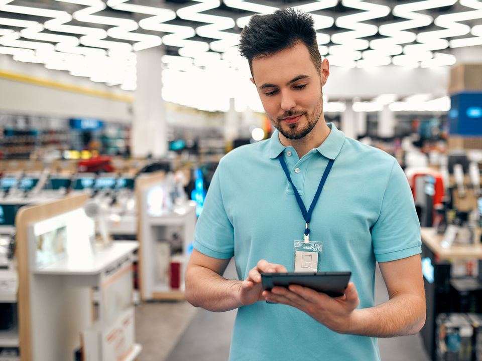 male retail associate reviewing store data on electronic tablet in store aisle