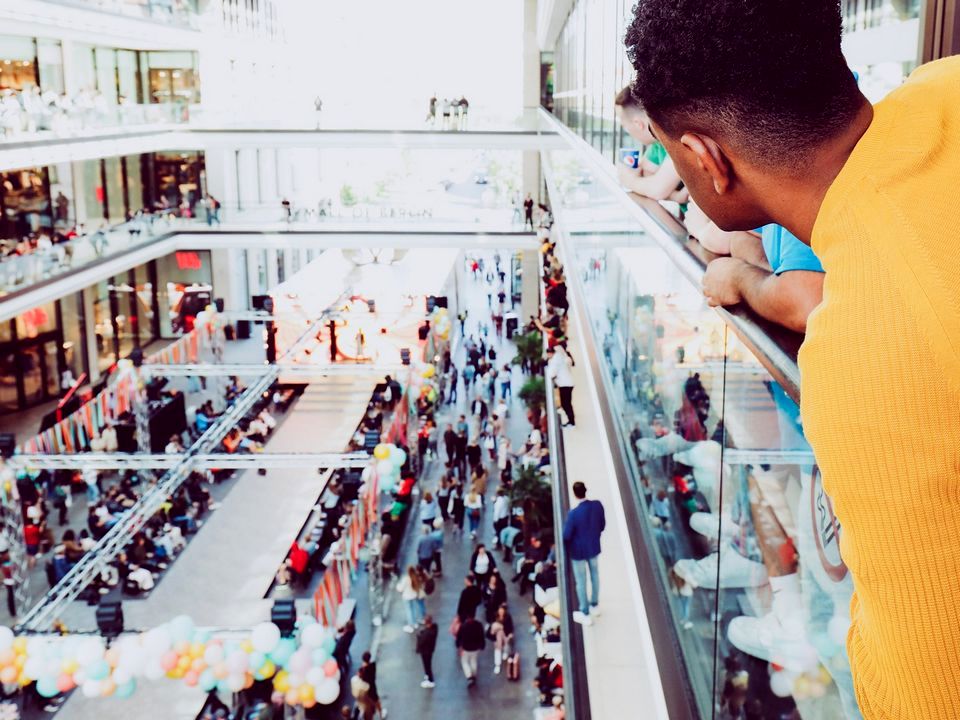 man shopping in multi-level retail mall looking for friend leans over the open atrium to the ground level